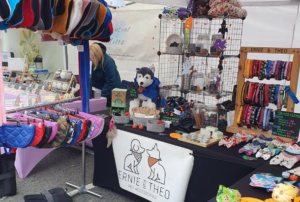 image showing dogs accessories set up on stall including an array of collars in various colours, brightly coloured quilted dog coats, and dog bow ties.