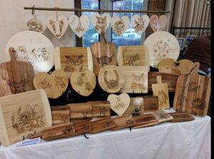 image of lots of wooden chopping boards, cheeseboards and grazing boards in various shapes and sizes set up on a craft stand table, each with a different lasered design such as animals, flowers and food and drink images.