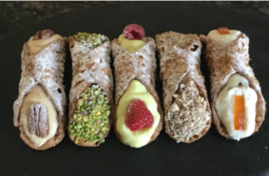 image of five cannoli dessert deep fried pastry tubes stuffed with sweetened ricotta and each one finished with different fruit and nut toppings.