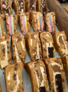 image of sliced cookie pies, containing white cream and chocolate chip fillings, other sliced cookie pies showing rainbow coloured cream fillings.