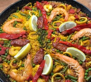 image of Spanish paella in a pan , consisting of golden rice, peas, chorizo, calamari , peppers and lemon wedges