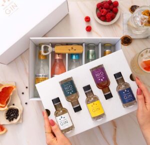 image of hands opening gift box of beutifully presented minature gin bottles, various fruits such as orange , raspberry neatly placed around the table.