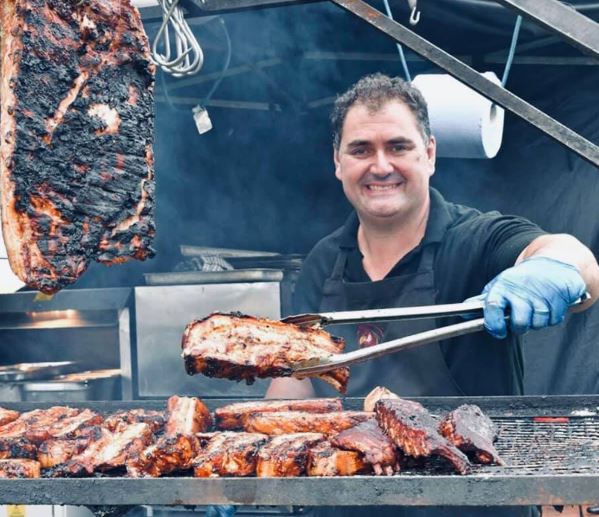 image of a man barbecuing meat at a stand. holding a piece of meat between a tong.