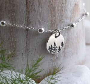 image of silver chain around piece of wood with silver circular disk in centre of chain showing etched images of forest trees.