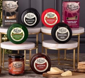 Image of various coloured wax truckle cheeses on stands with two boxes of crackers and chilli jam in image.